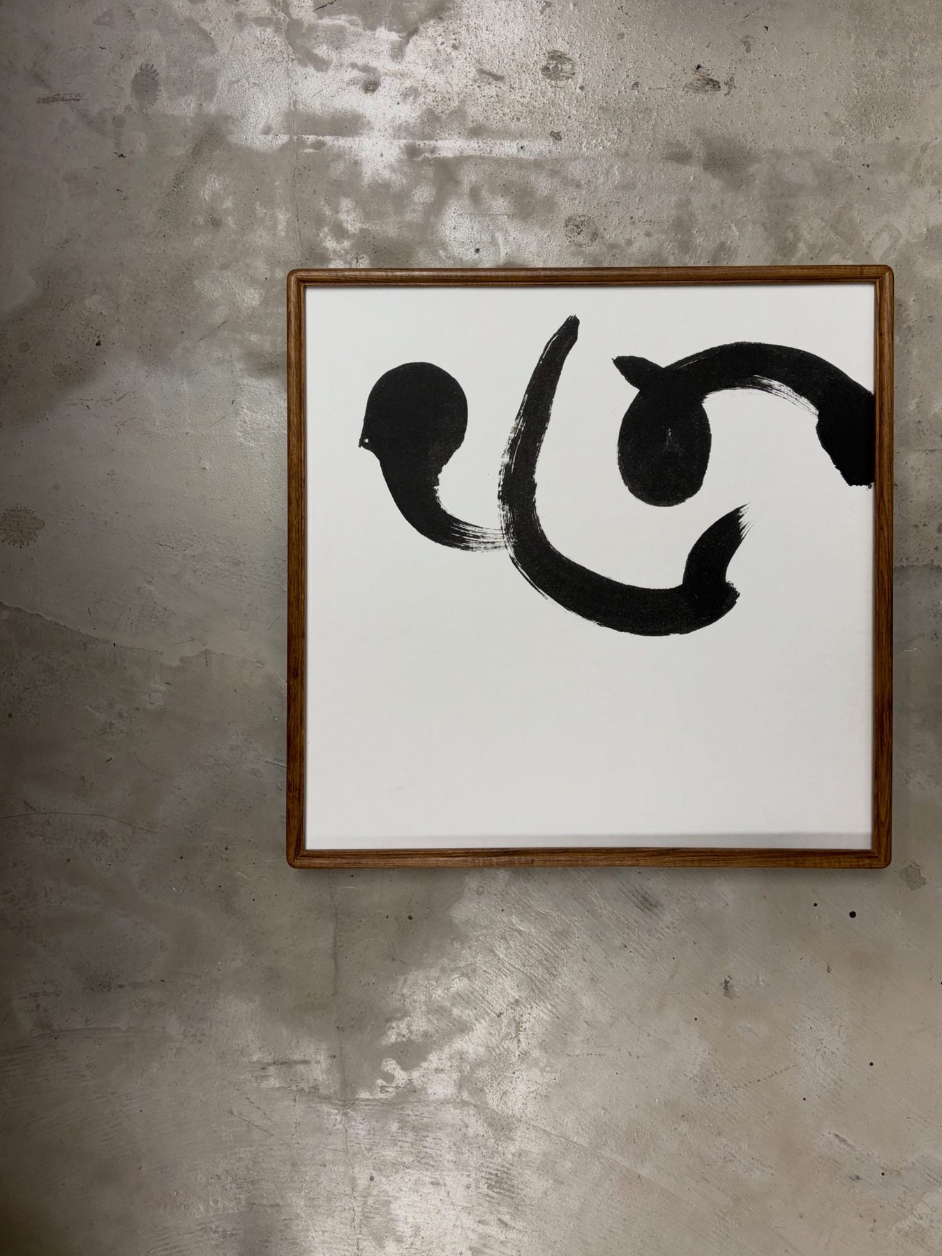心 — Heart. A single sweeping character framed in wood against a raw concrete wall.